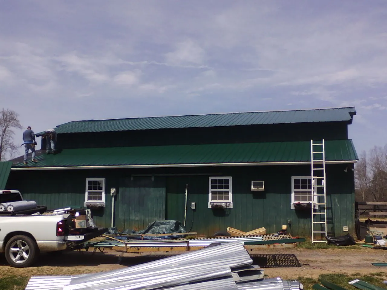 Crew installing green metal roofing on a large green barn in Hamilton